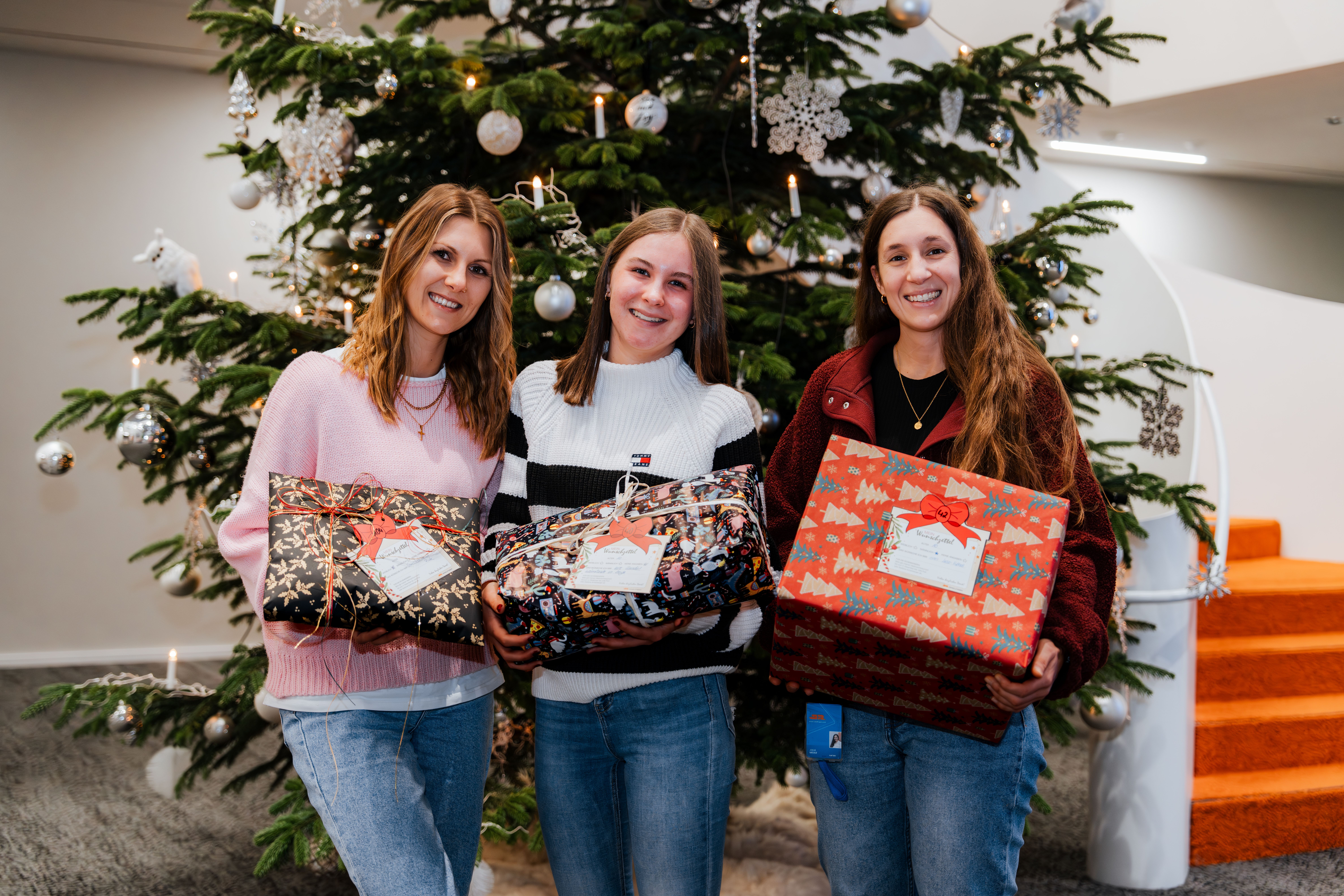 Die drei Organisatorinnen der Wunschbaum-Aktion vor dem Weihnachtsbaum im Atrium der Chamer Hauptverwaltung mit jeweils einem der Geschenke.