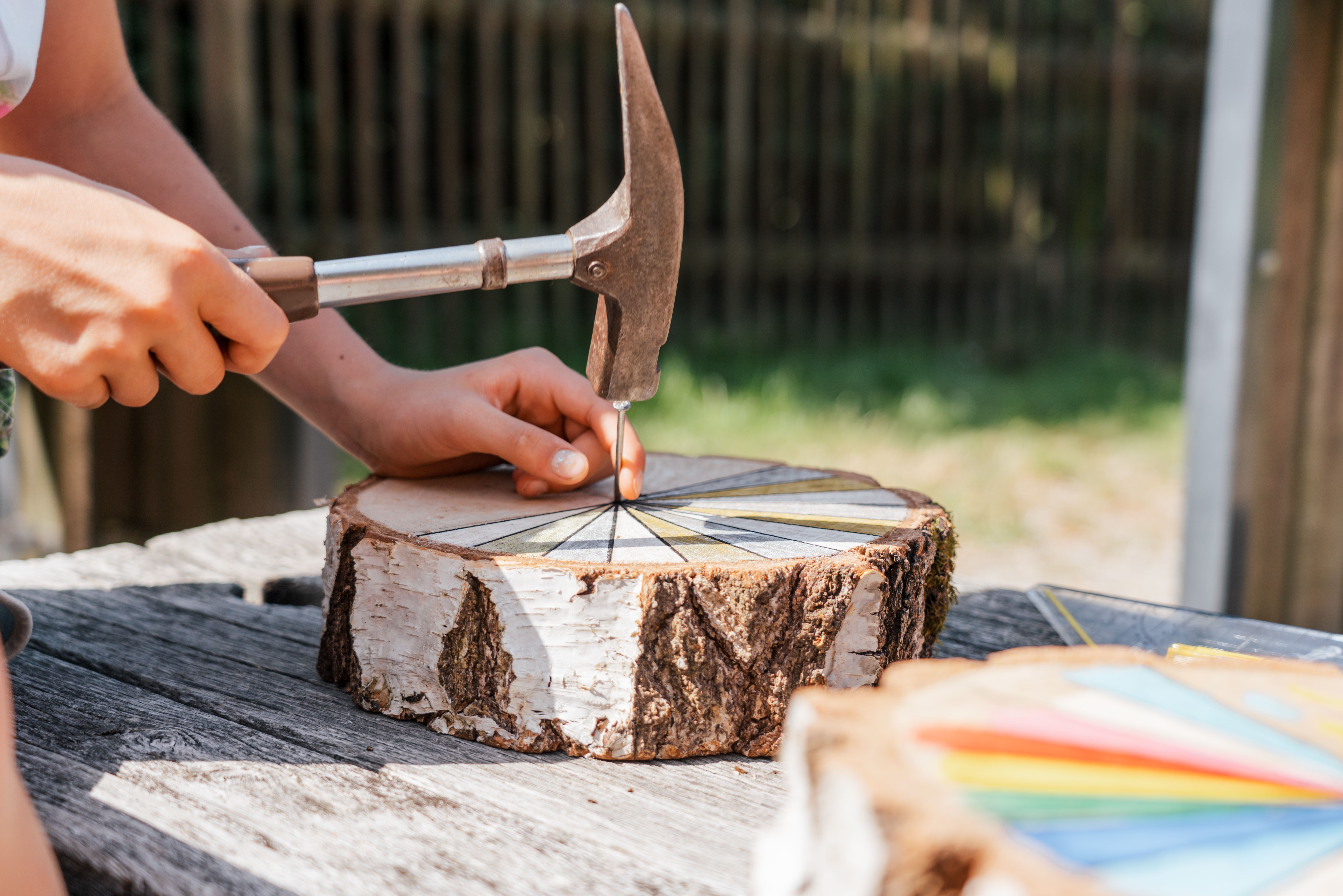 Person baut eine Sonnenuhr und hämmert einen Nagel in ein buntes Holzrad, Detailaufnahme