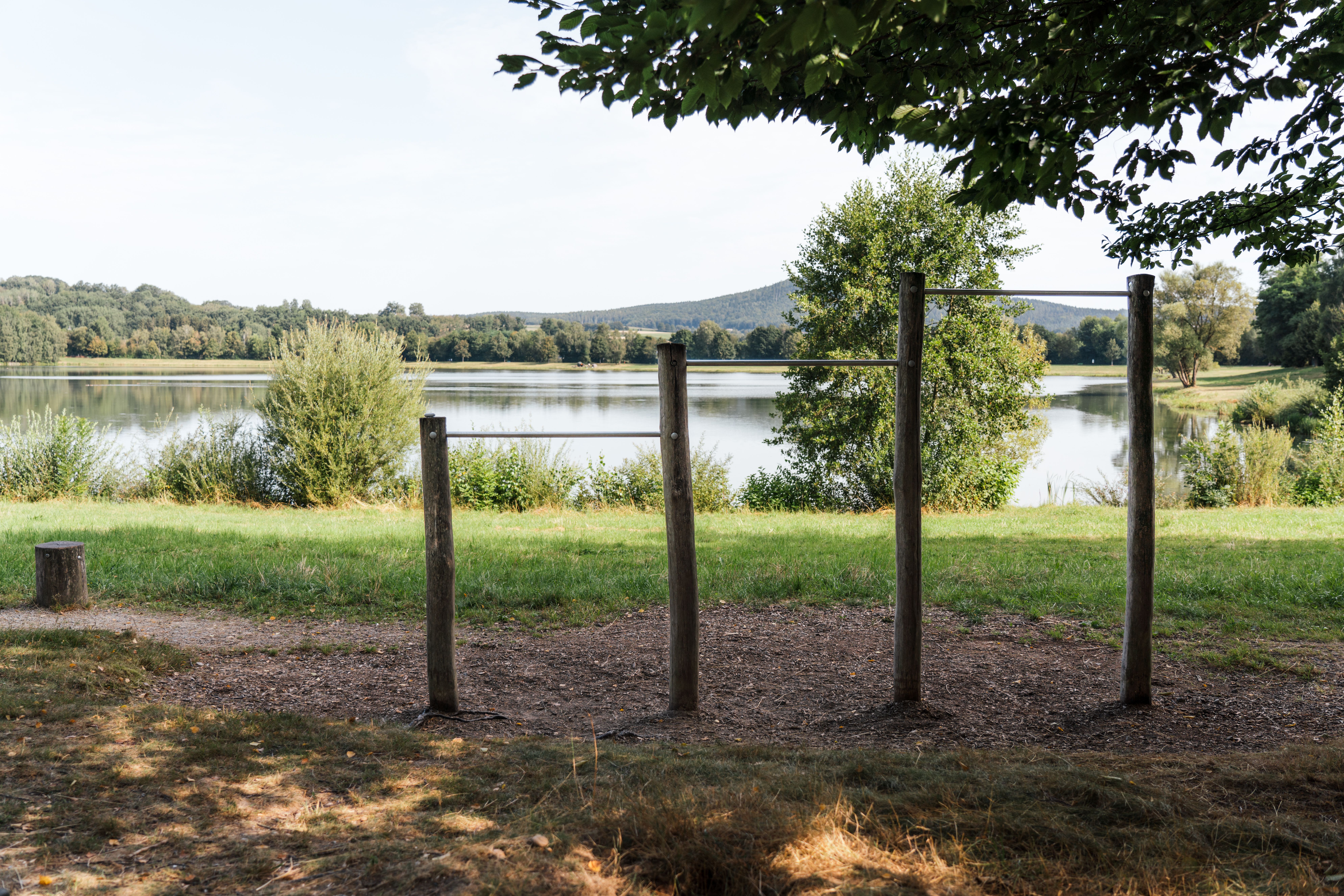 Platz der Bewegung am Satzdorfer See: Outdoor-Fitnessgerät aus Holz und Metall am Seeufer, umgeben von Natur