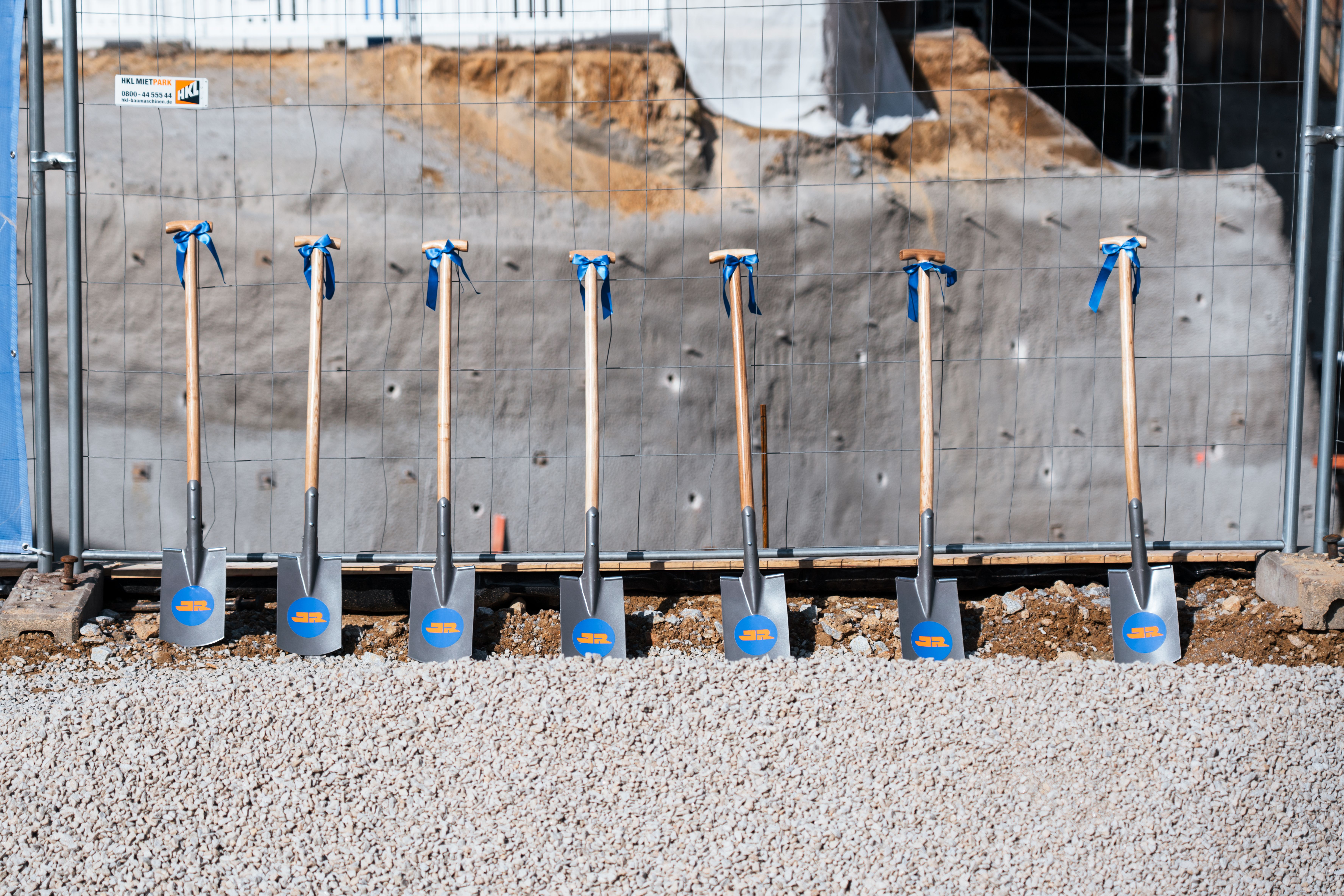 Schaufeln mit JR Logo lehnen am Bauzaun der Baustelle