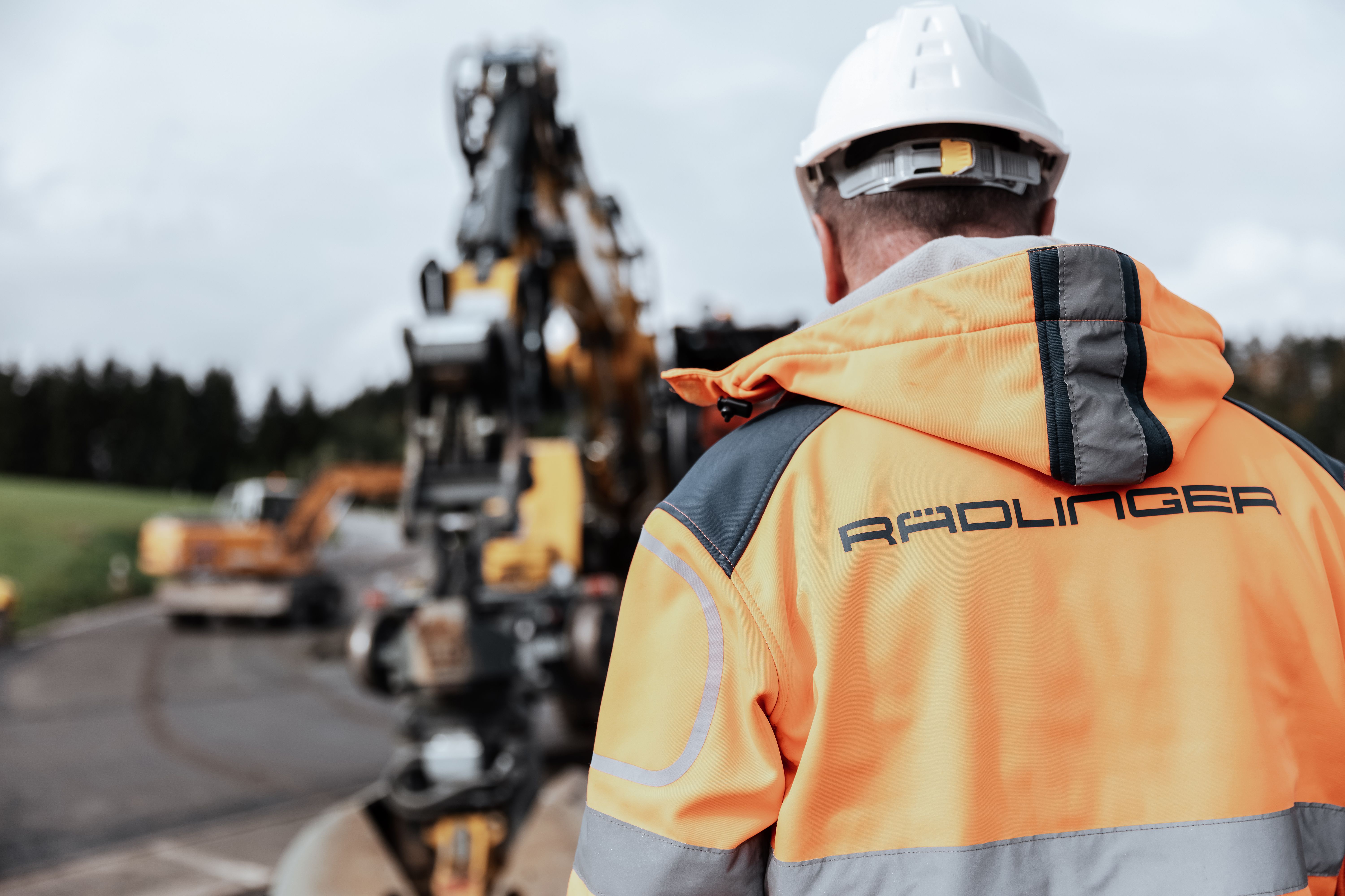 Rädlinger Mitarbeiter mit Bauhelm und Warnjacke auf Baustelle von hinten