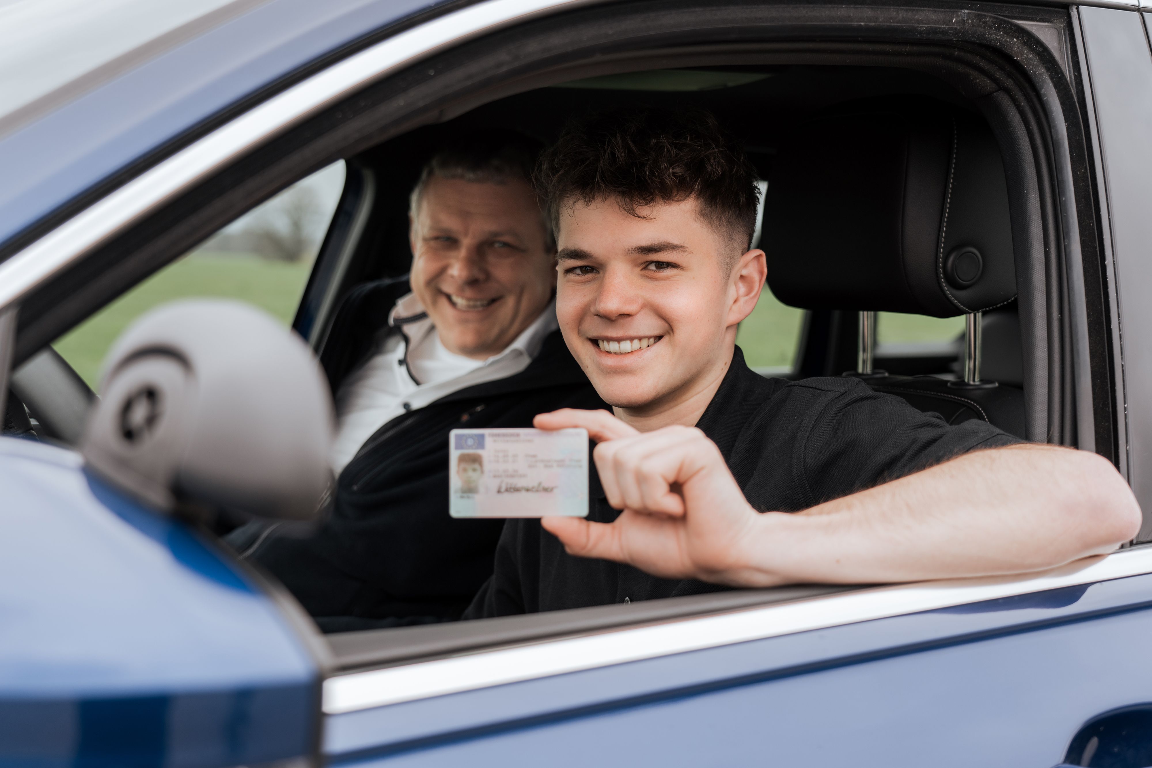 Azubi mit Fahrlehrer im Fahrschulauto der JR Verkehrsakademie, Azubi hält Führerschein in der Hand